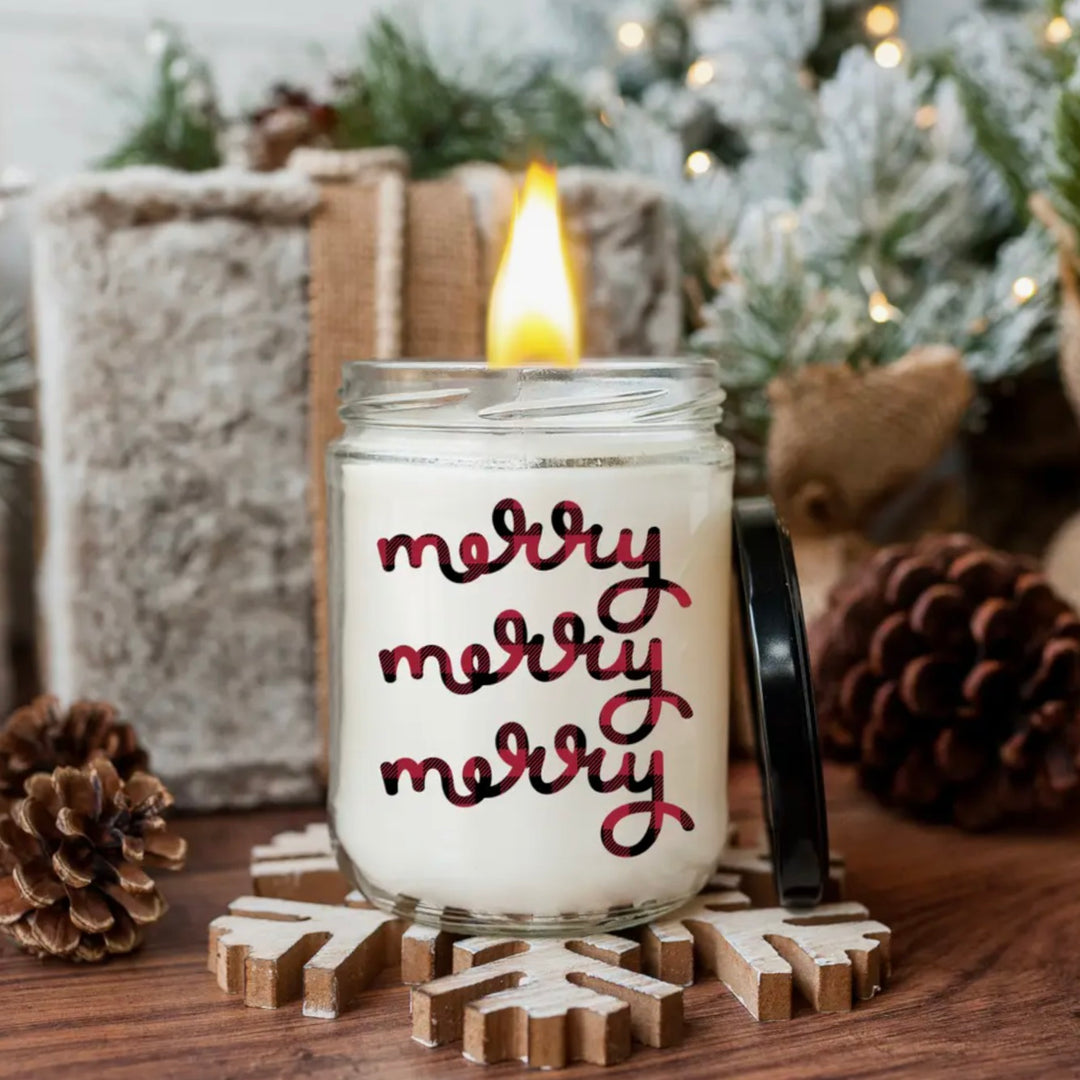 A Christmas Baking Scented Candle with 'Merry Merry' text on the label, placed on a wooden surface with pine cones and decorative items in the background, indicating a Christmas-themed setting.