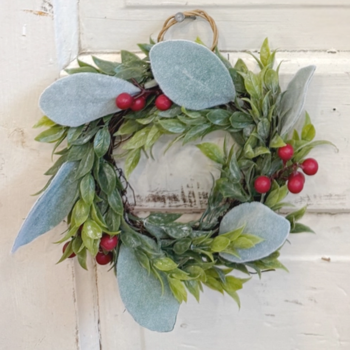 Decorative wreath with green leaves and red berries on a white wooden background