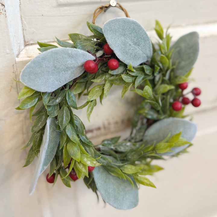 Decorative wreath with green leaves and red berries on a neutral background
