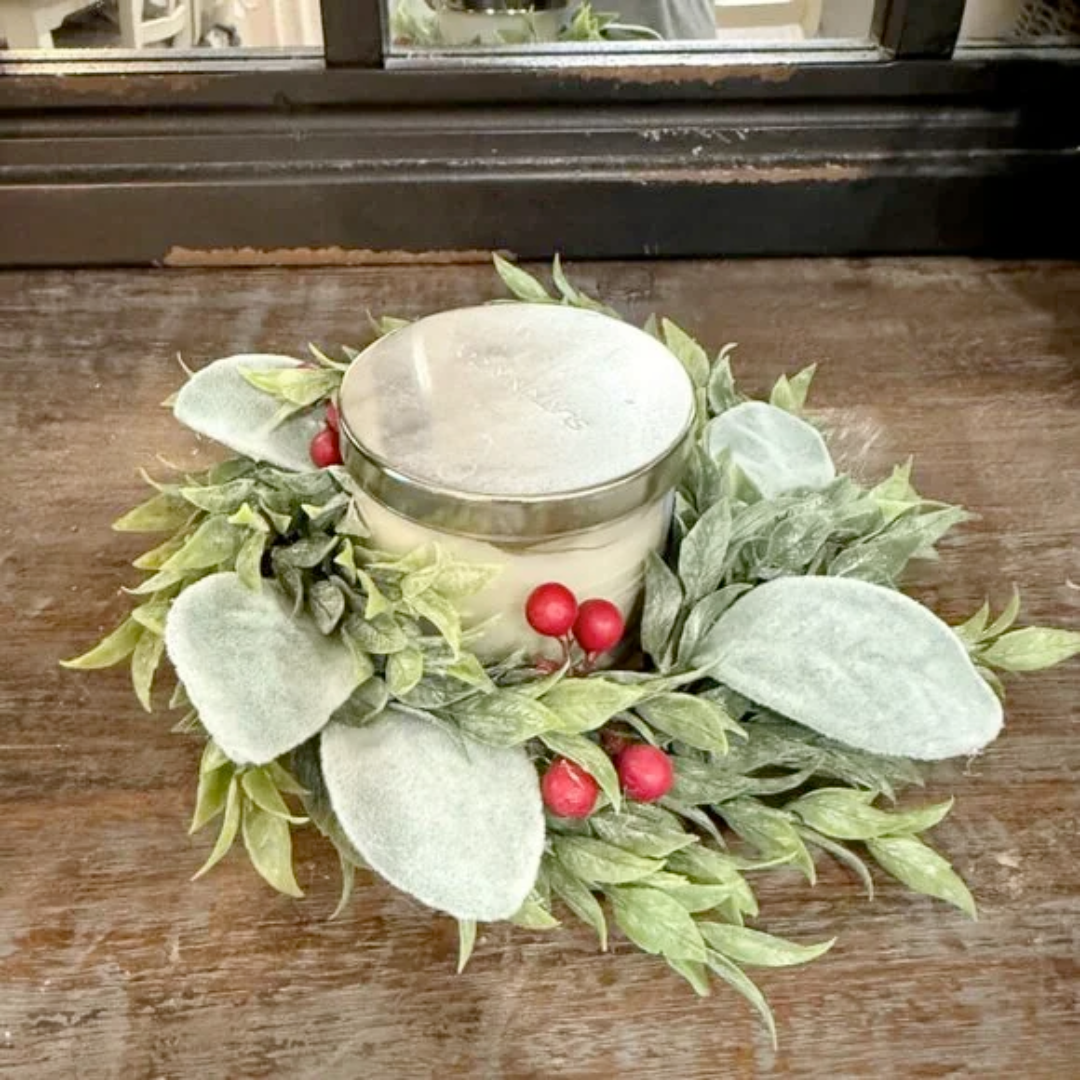 Candle in a decorative holder with green leaves and red berries on a wooden surface.