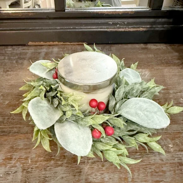 Candle in a decorative holder with green leaves and red berries on a wooden surface.