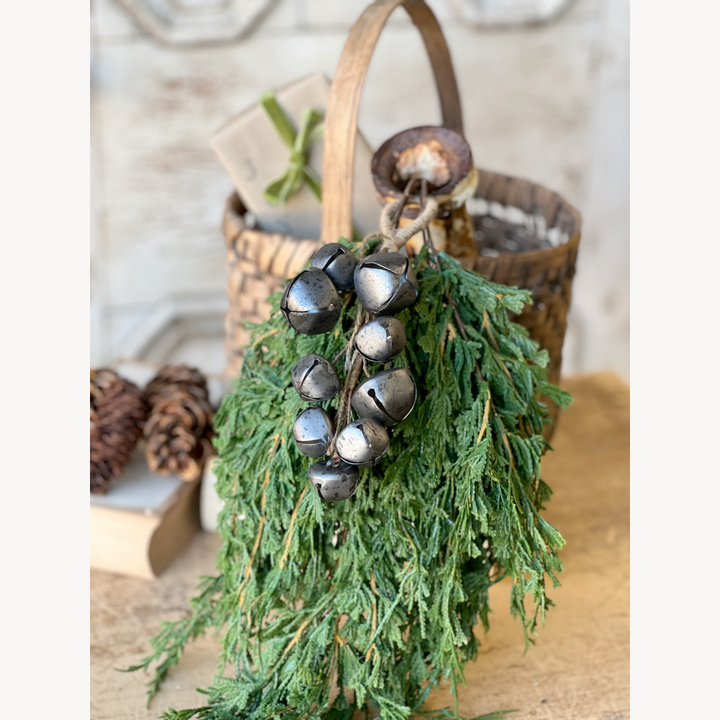 Decorative hanging with greenery and metal bells on a wooden surface.
