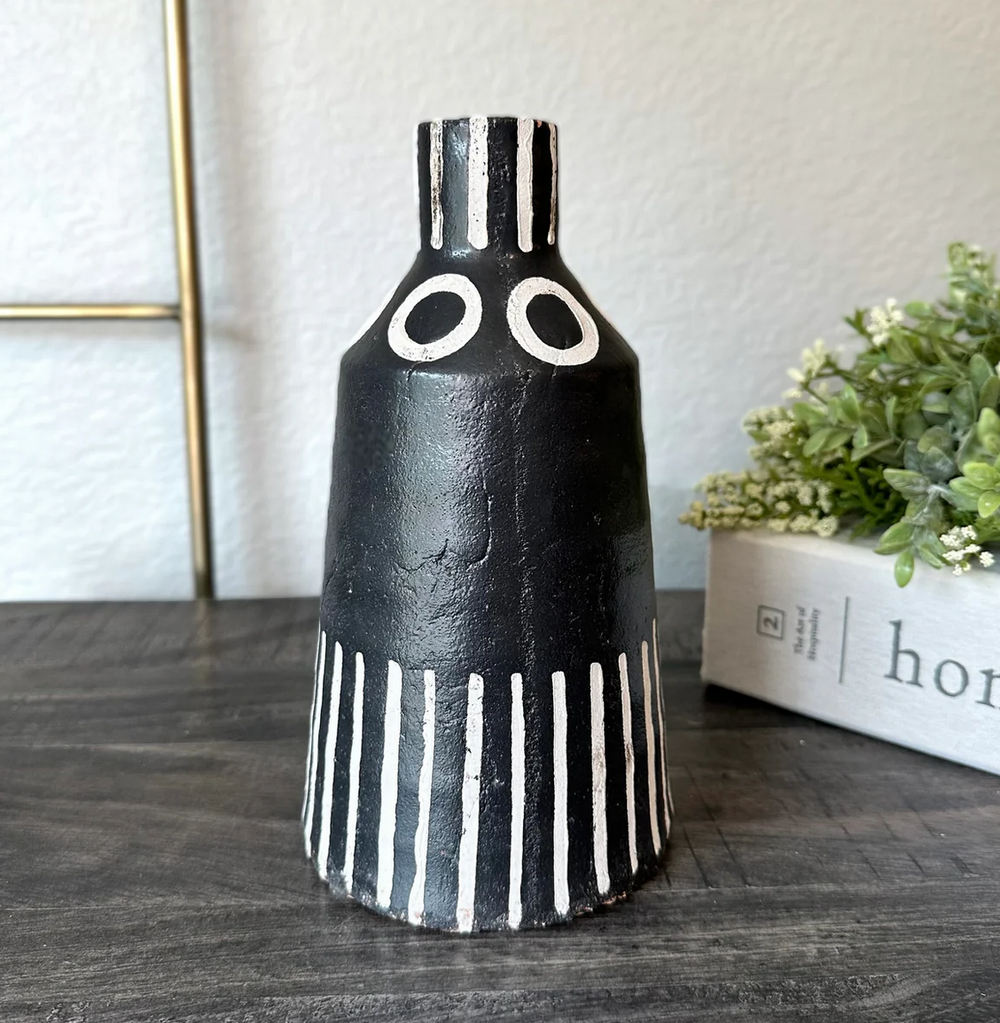 Black and white striped vase on a wooden surface with a plant in the background
