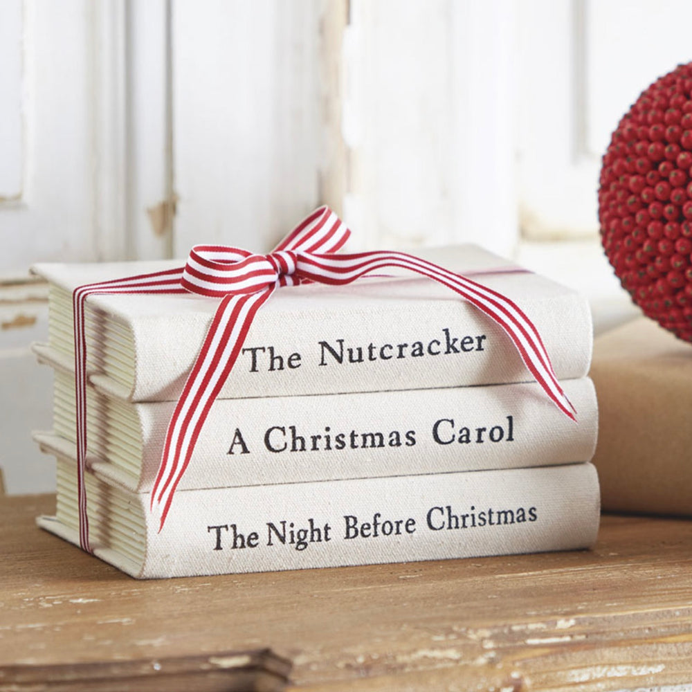 Stack of books titled 'The Nutcracker', 'A Christmas Carol', and 'The Night Before Christmas' tied with a red and white striped ribbon.