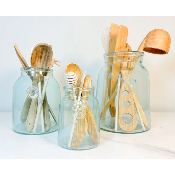 Three glass mason jars filled with wooden kitchen utensils on a white background