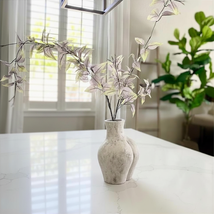 White Culo vase with decorative branches on a marble surface in a bright room.