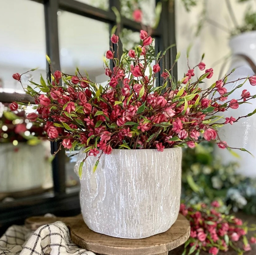 White textured concrete pot with red flowers on a wooden stand