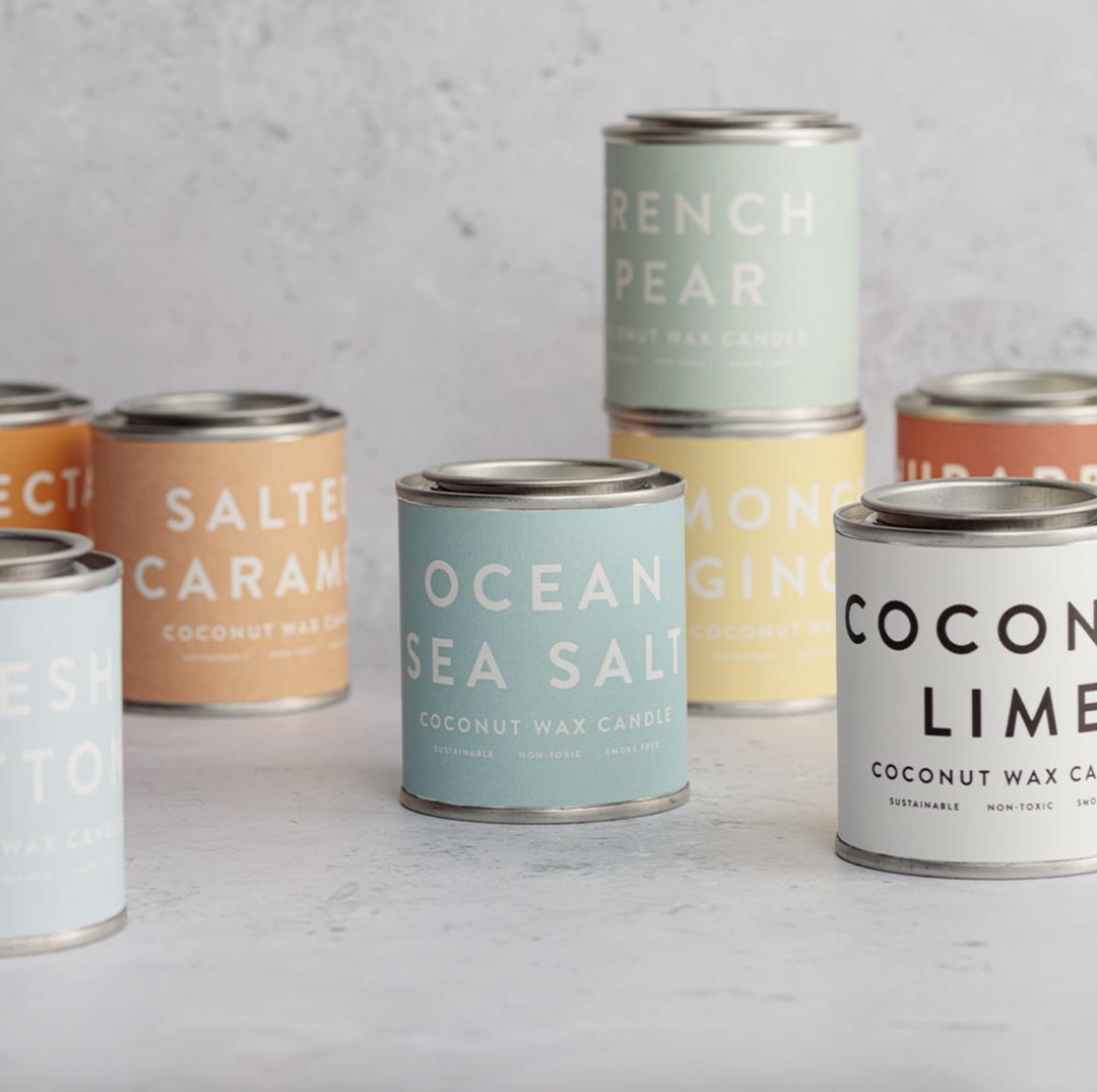 A collection of Conscious Coconut Wax Candles in various colors, displayed in reusable and recyclable paint tins.