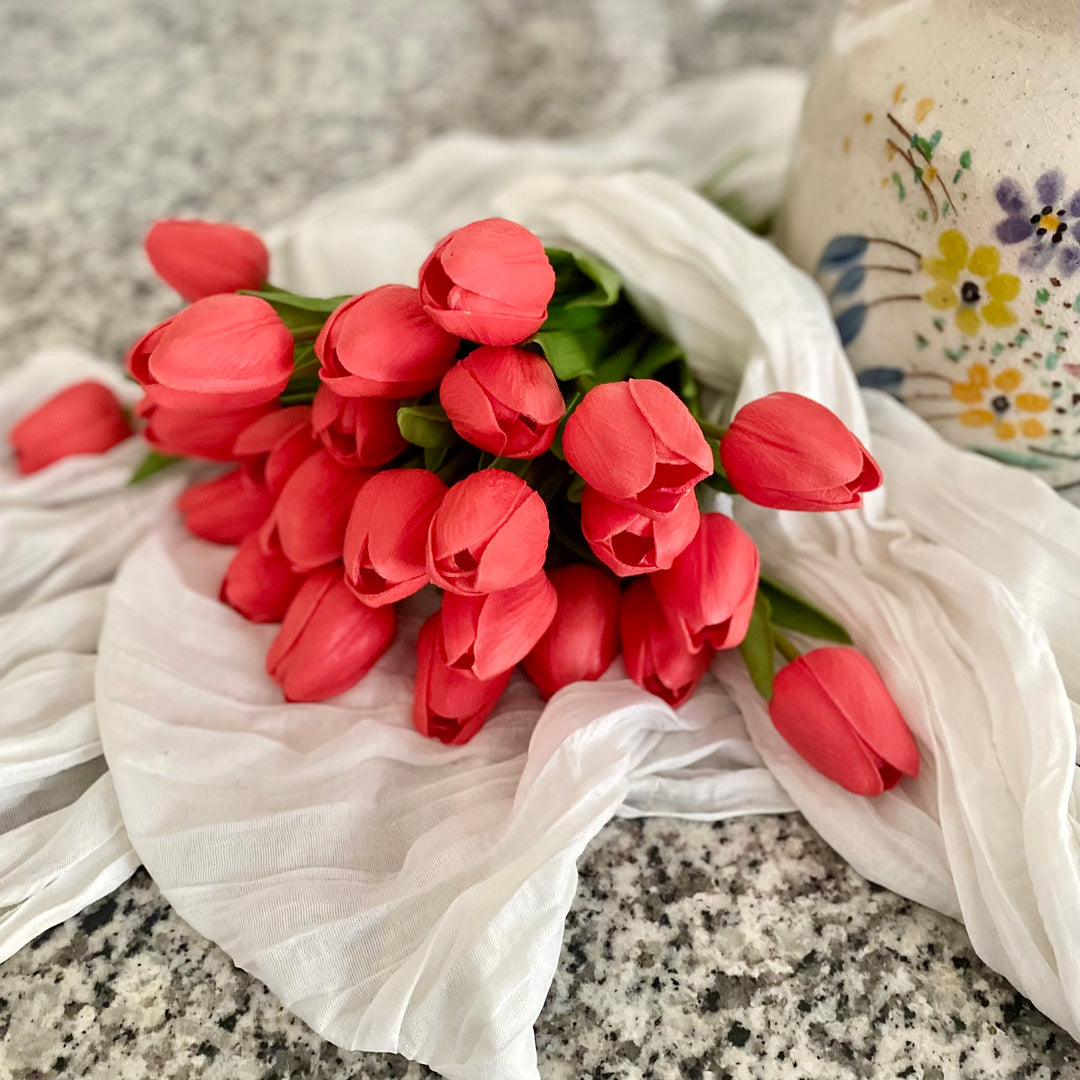 A bundle of artificial coral tulips tied with paper bows, arranged on a surface with a terracotta pitcher in the background.
