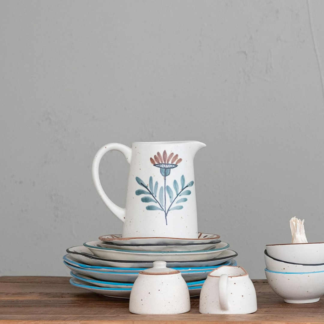 Stoneware pitcher with floral design on a wooden table against a gray background