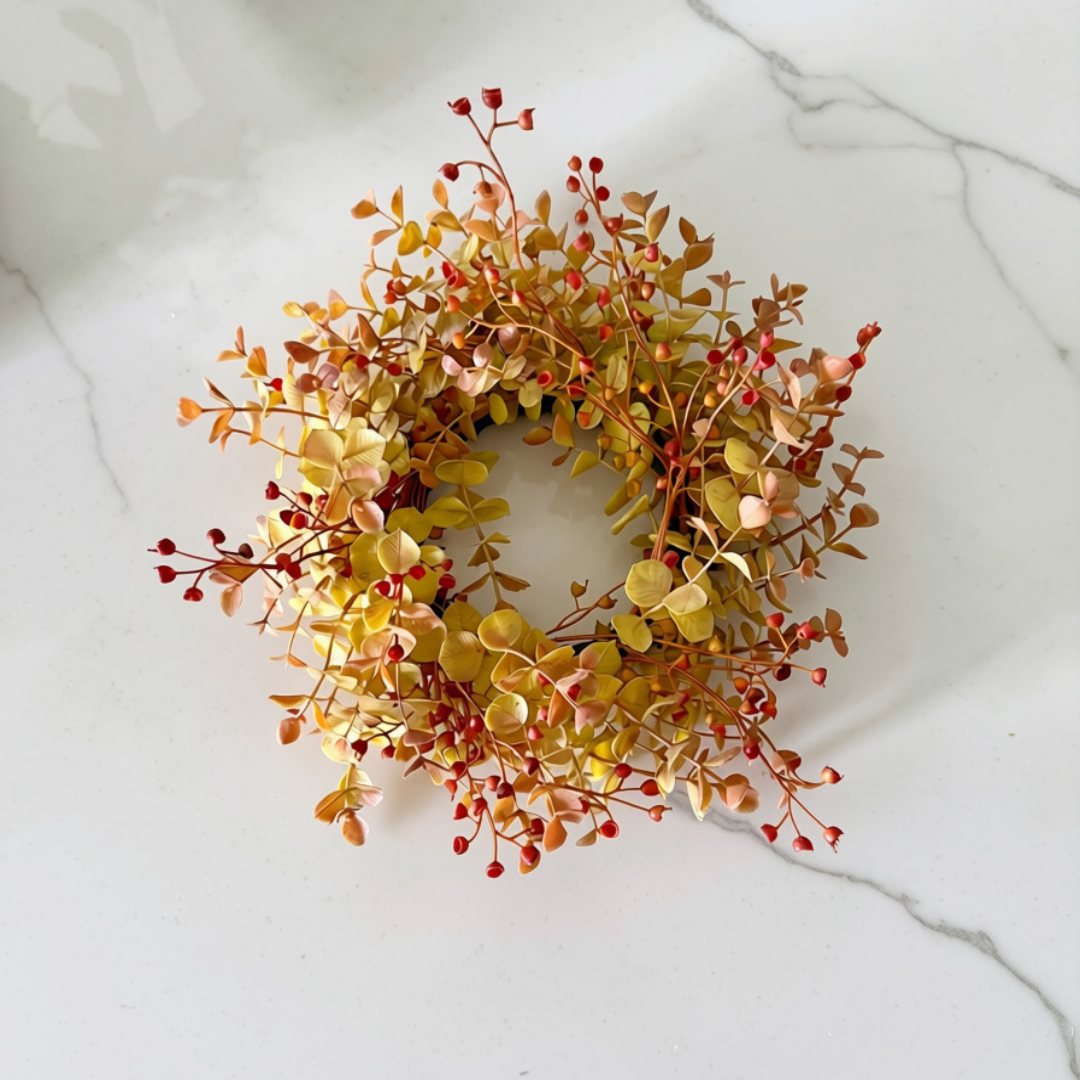 An autumn-themed artificial wreath with yellow, orange, and red leaves and berries, displayed on a white marble surface.