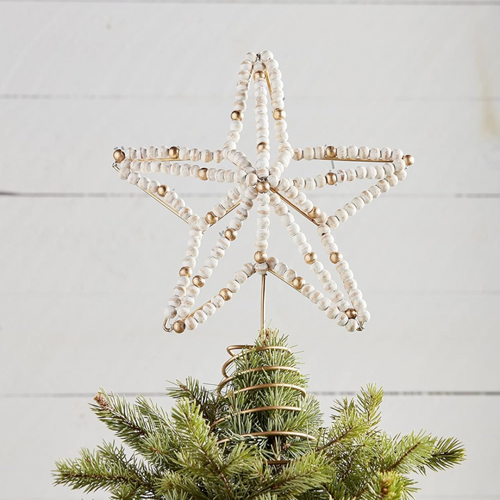 Decorative star tree topper with beads on a Christmas tree against a light wooden background