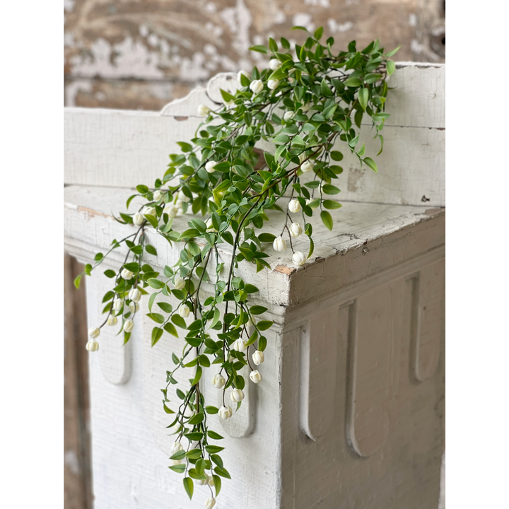 Decorative green vine with small white flowers on a rustic wooden surface