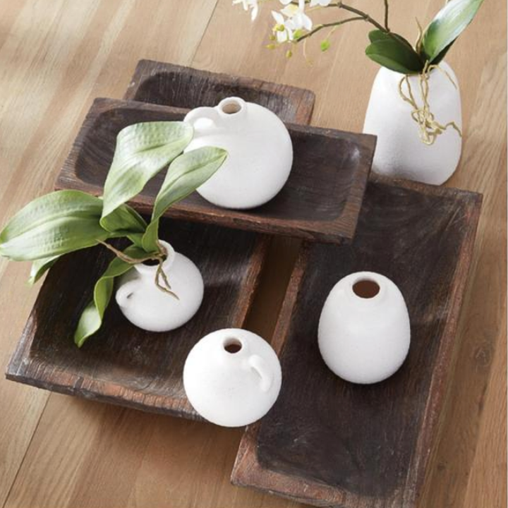 White ceramic vases on wooden trays with greenery