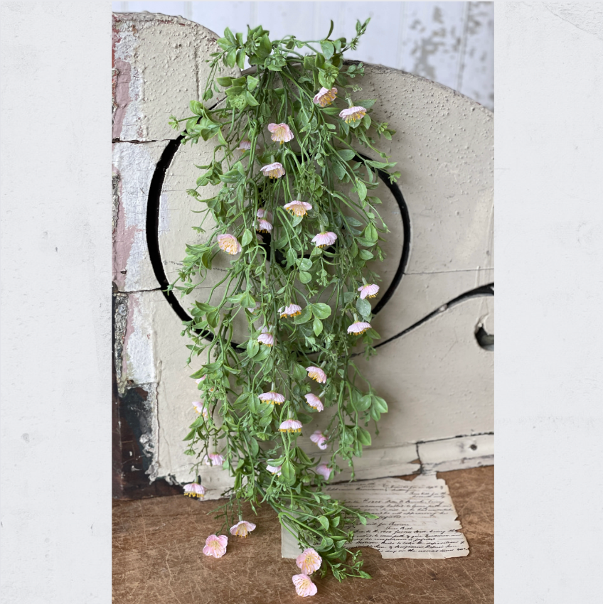 Artificial draping pink primrose plant with green leaves and pink flowers, displayed against a rustic background.