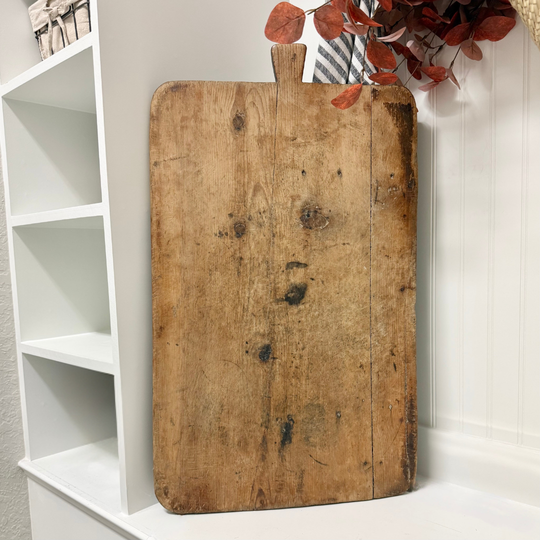 Vintage wooden cutting board with a white shelf and decorative leaves in the background