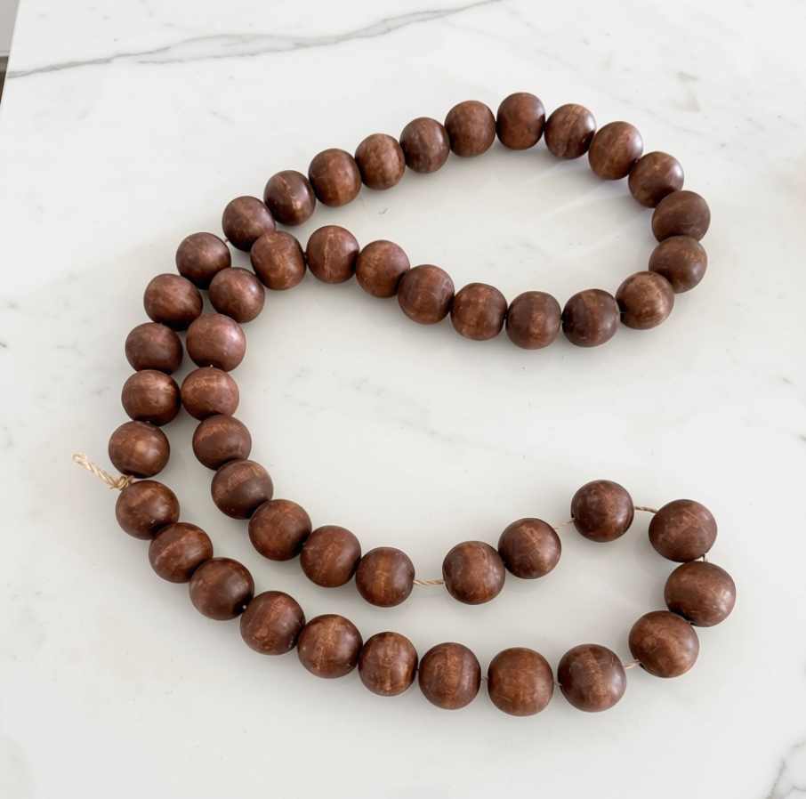A strand of medium brown wooden beads with a natural wood grain finish, laid out in a loose loop on a white marble surface.