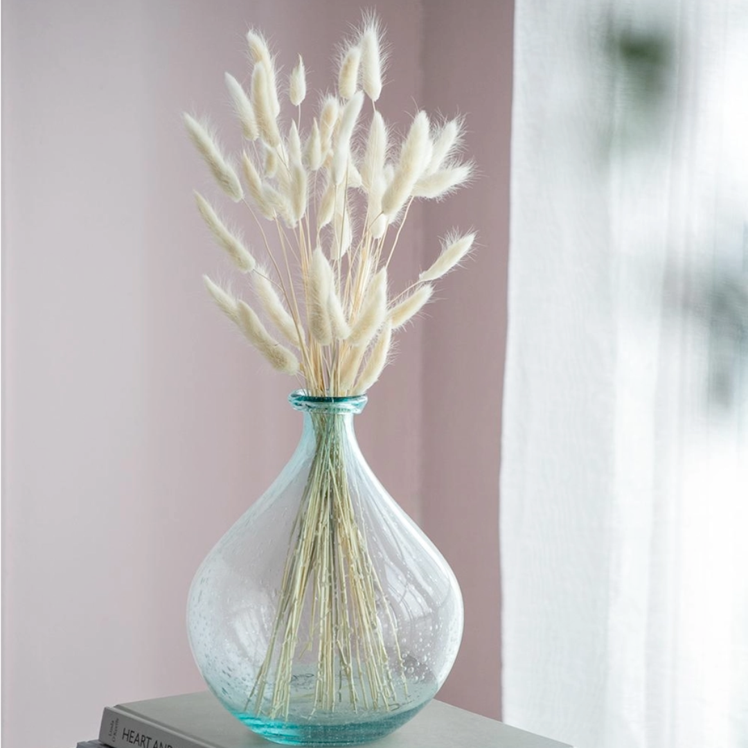 Turquoise vase with dried grasses on a surface against a pink wall