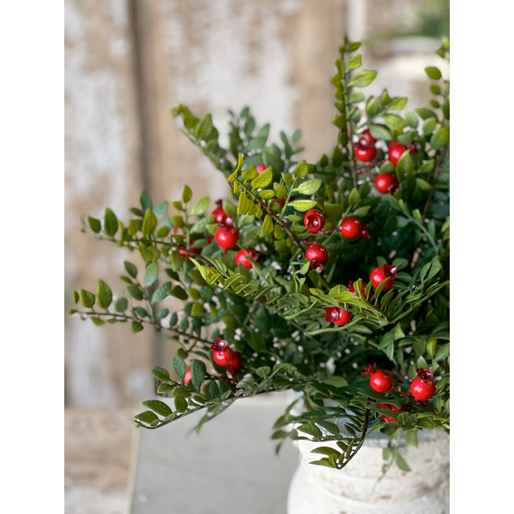 Artificial green plant with red berries in a white pot against a neutral background