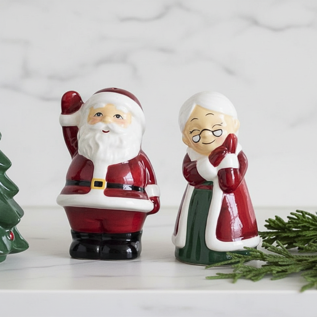 Decorative salt and pepper shakers shaped like Santa Claus and Mrs. Claus on a white surface with a Christmas tree.