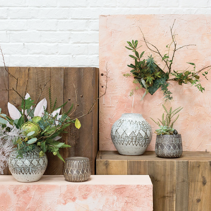 Decorative vases and plants on a wooden shelf with a textured wall background