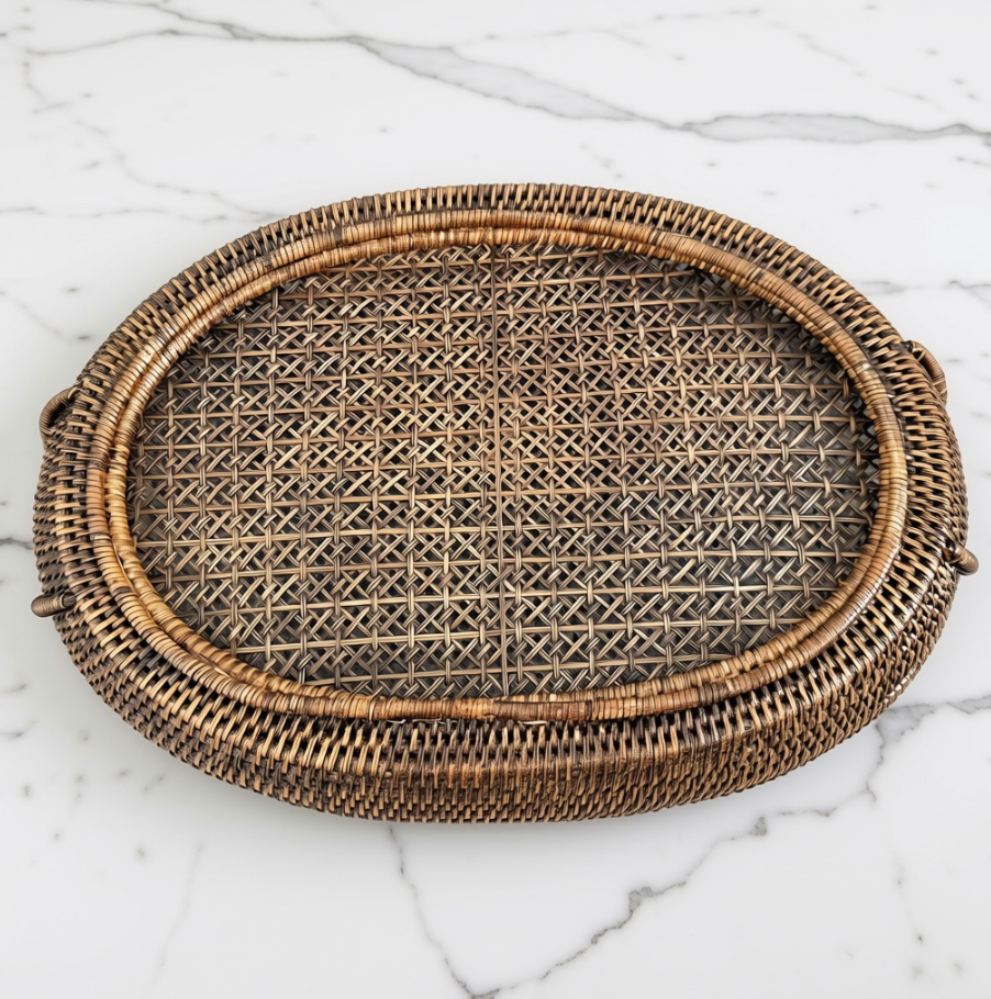 An oval woven rattan tray with a natural brown and beige textured weave, displayed on a white marble surface.