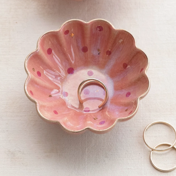 Pink flower-shaped stoneware dish with gold details displayed on a surface with two small rings lying beside the larger dish.