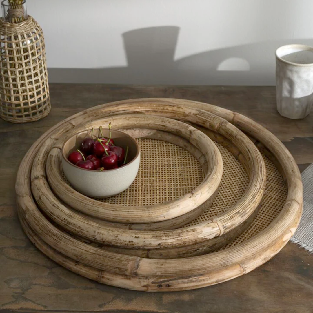 Set of round woven trays on a table with a bowl of cherries.
