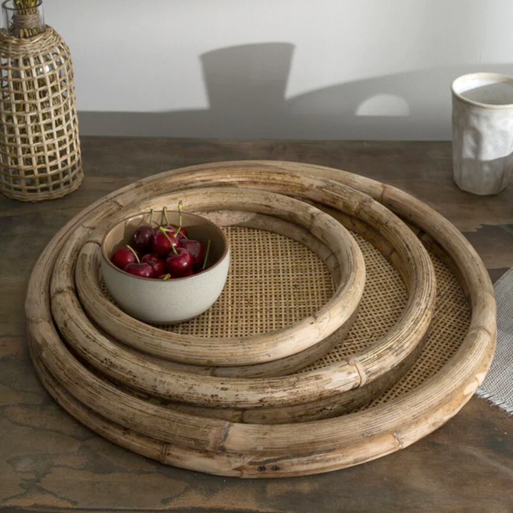 Set of round woven trays on a table with a bowl of cherries.