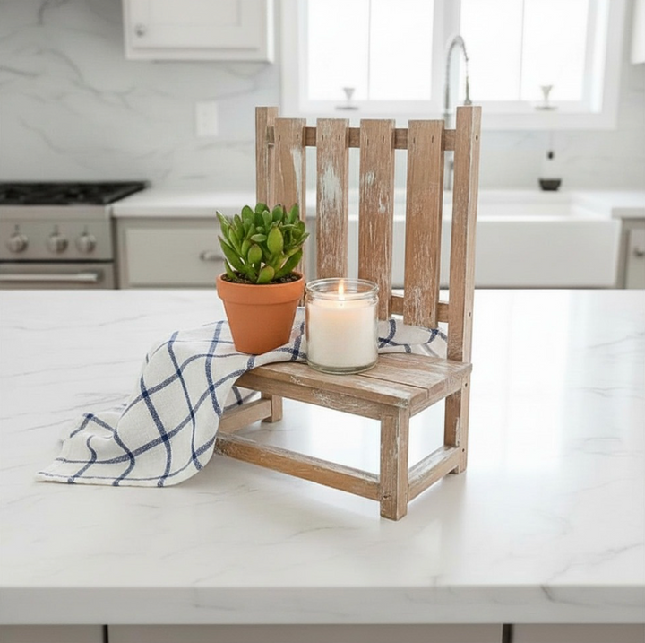 A rustic wooden pallet-style plant stand bench decoration sits on a white marble kitchen island, styled with a small potted succulent, a white candle in a glass jar, and a blue-and-white checkered cloth.