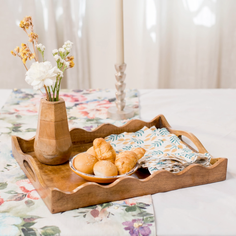Mango Wood tray with bread, a vase of flowers, and a folded cloth on a floral tablecloth.