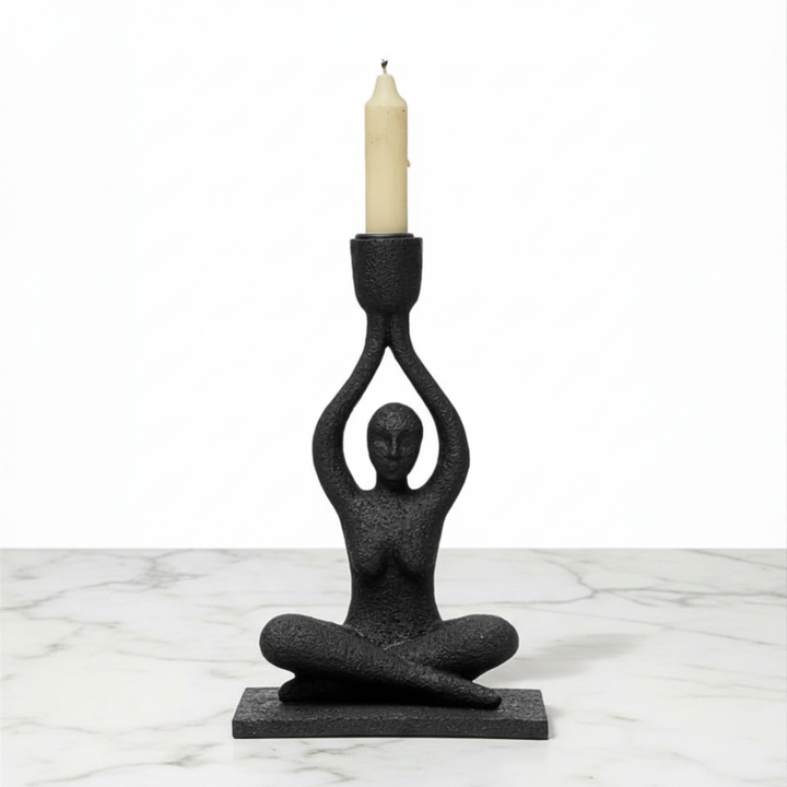 Black candle holder shaped like a person holding a candle on a marble surface