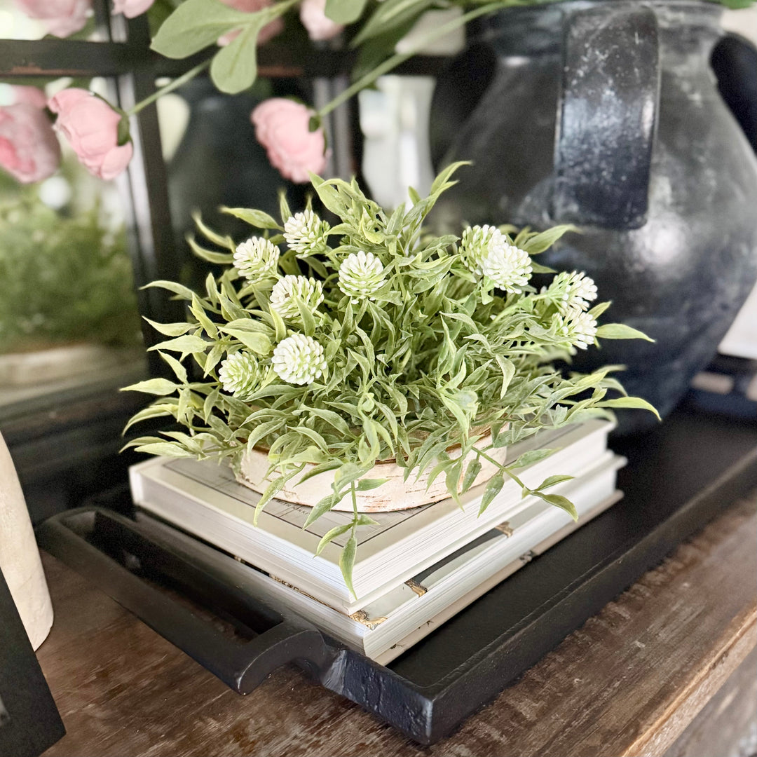 Decorative greenery half sphere with white flowers on a stack of books with a blurred background
