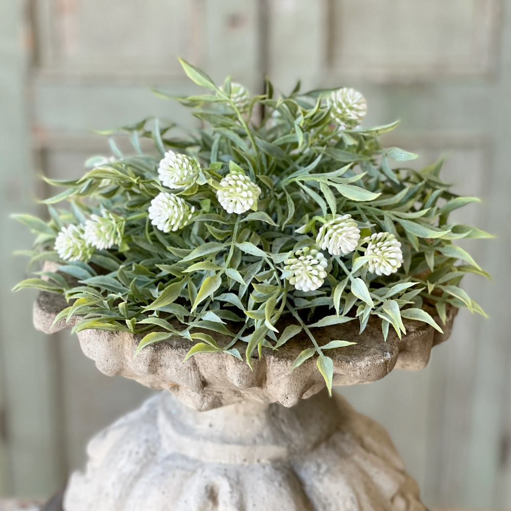Faux floral arrangement in a decorative stone planter against a neutral background