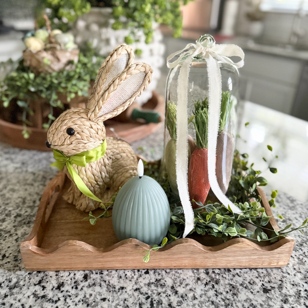 Decorative Easter display with a rabbit, flameless egg candle, and glass jar on a wooden tray.