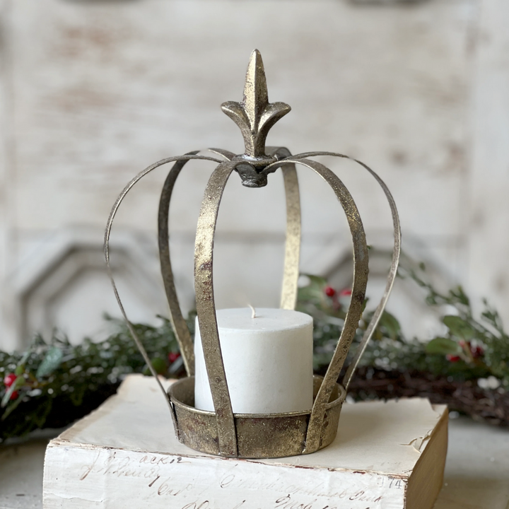 Decorative metal crown-shaped candle holder with a white candle on a wooden block.