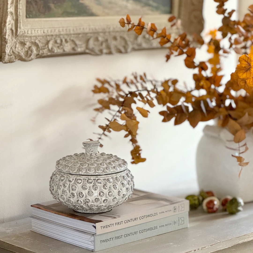 Decorative white pot on books with a vase of dried flowers in the background