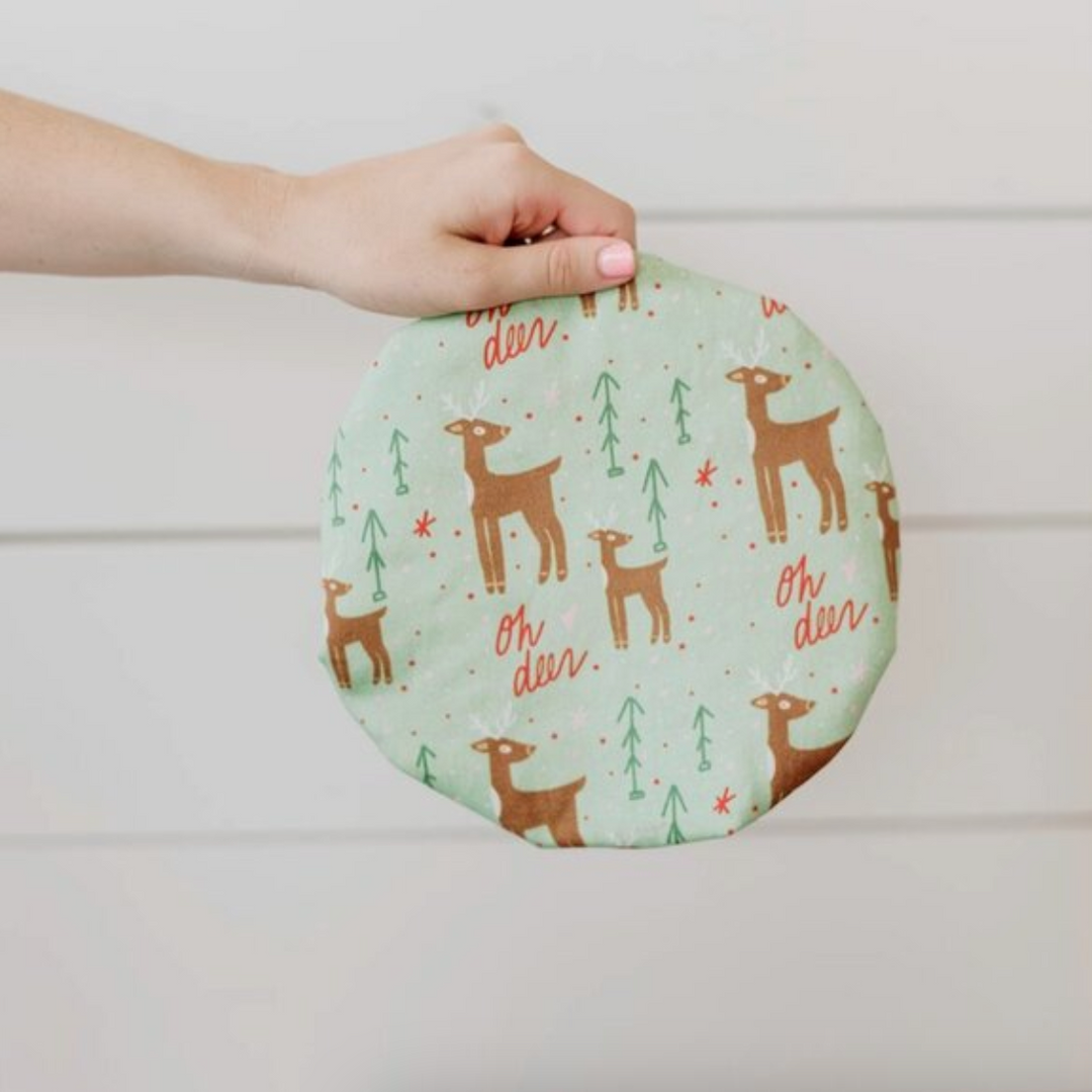 Round fabric bowl cover with deer pattern held by a hand against a neutral background