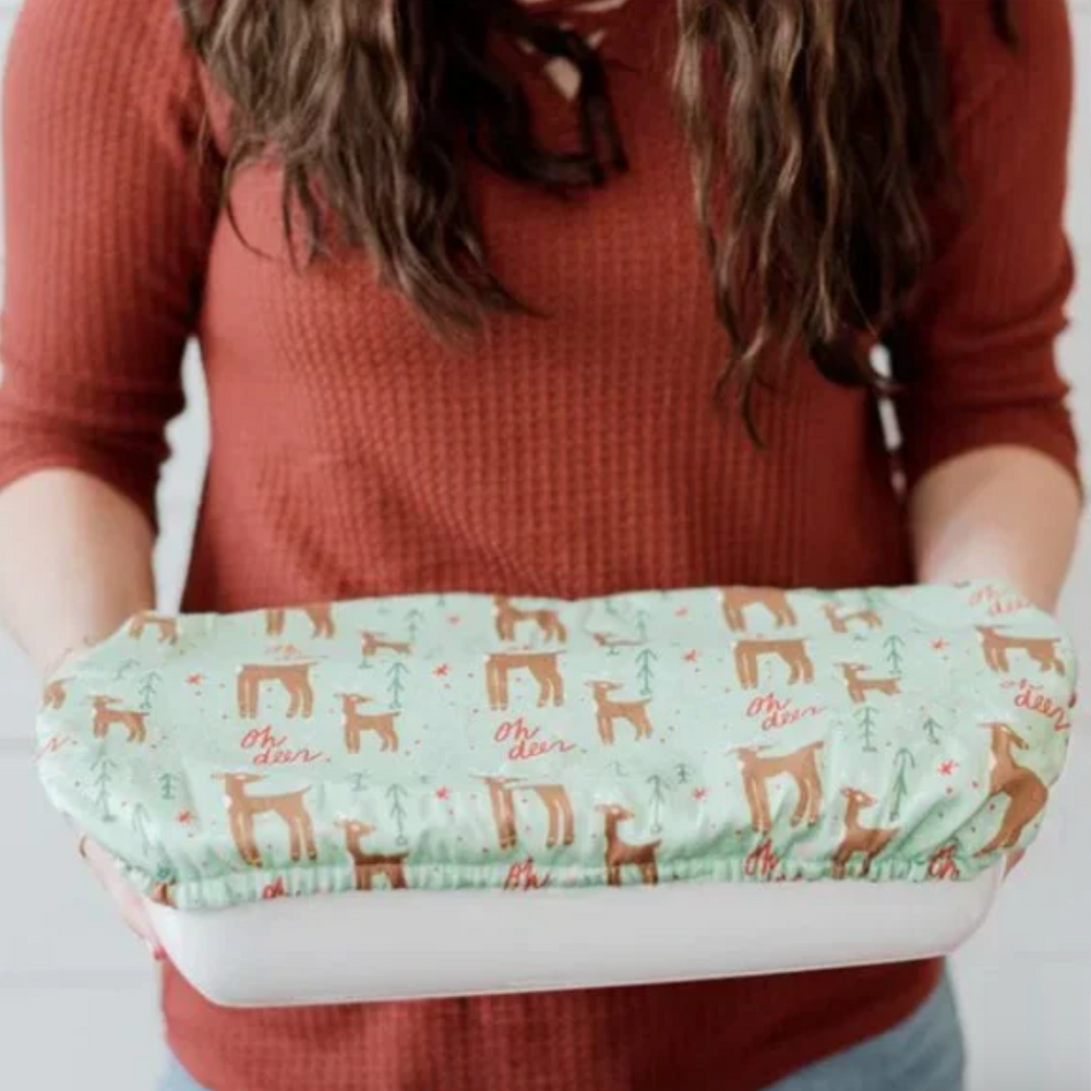 Person holding a white container with a green fabric bowl cover featuring a deer pattern