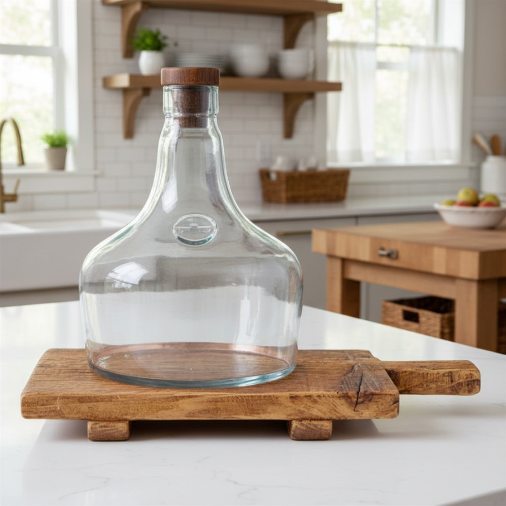 Clear glass demijohn cloche with wooden lid on a wooden stand in a kitchen setting