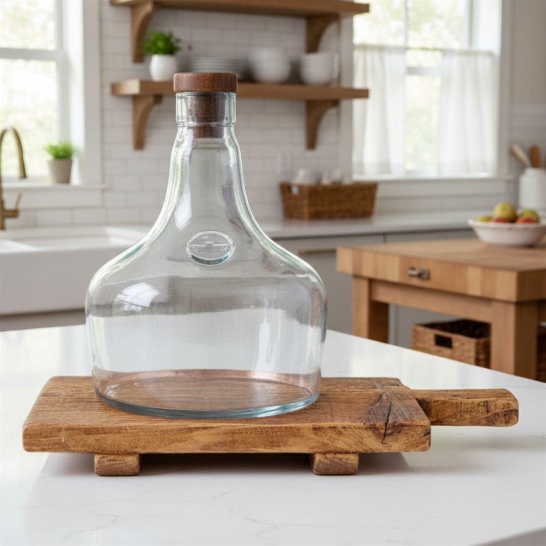 Clear glass demijohn cloche with wooden lid on a wooden stand in a kitchen setting