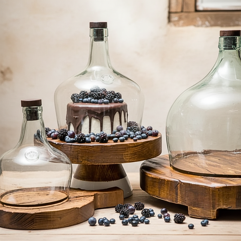 Glass bottles with wooden bases and a cake on a wooden stand with berries.