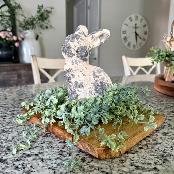 Decorative stone rabbit on a wooden board with greenery on a kitchen counter.