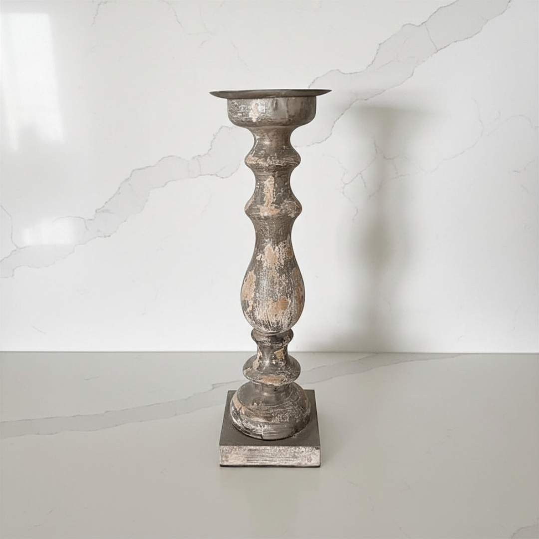 A distressed and textured mud brown finish candlestick holder with a square base, standing on a light gray surface against a white marble-patterned background.
