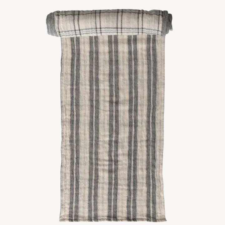 A cream and gray striped cotton table runner rolled up at one end, displaying a plaid pattern.