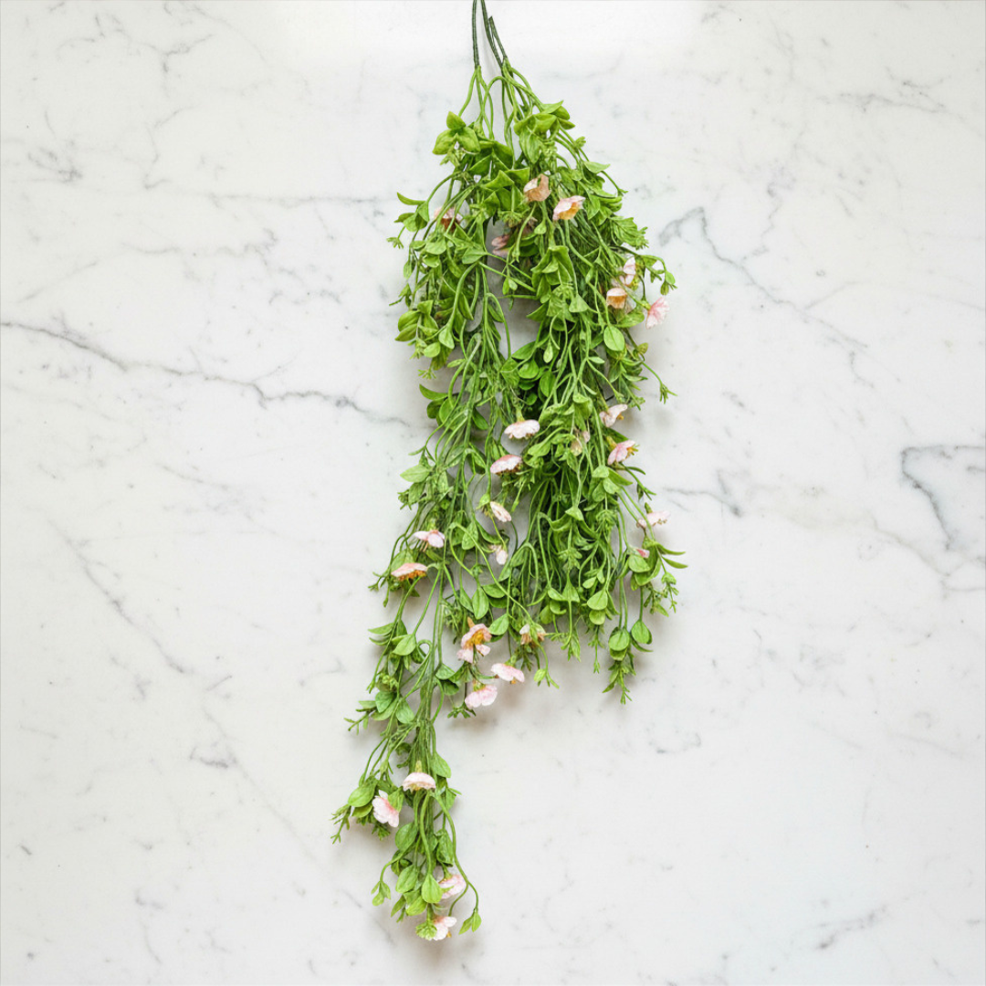 Hanging green plant with small pink flowers on a marble surface