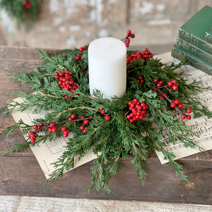 Decorative arrangement with greenery, red berries, and a white candle on a wooden surface.