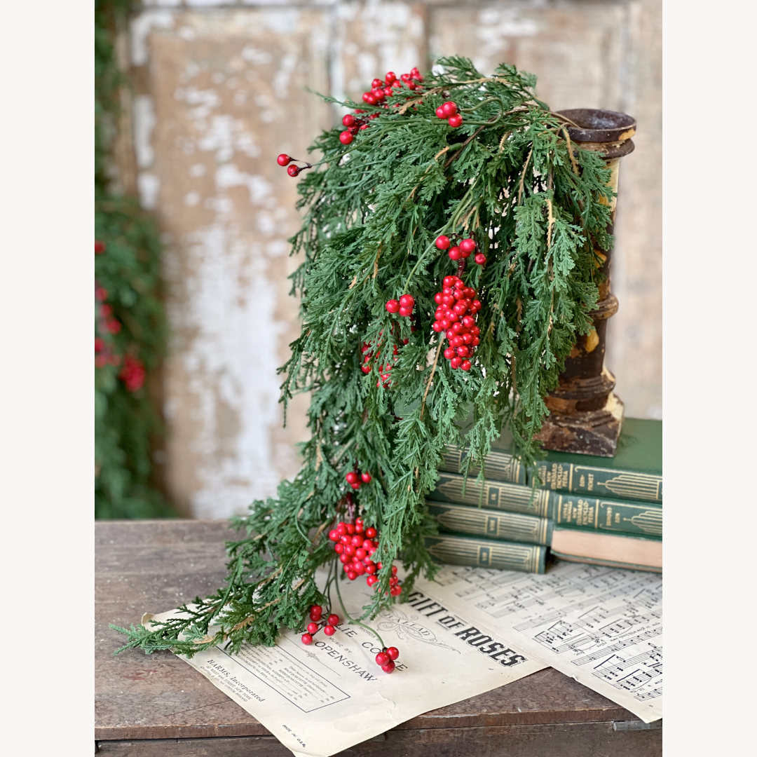 Decorative green garland with red berries on a rustic surface with books and newspaper.