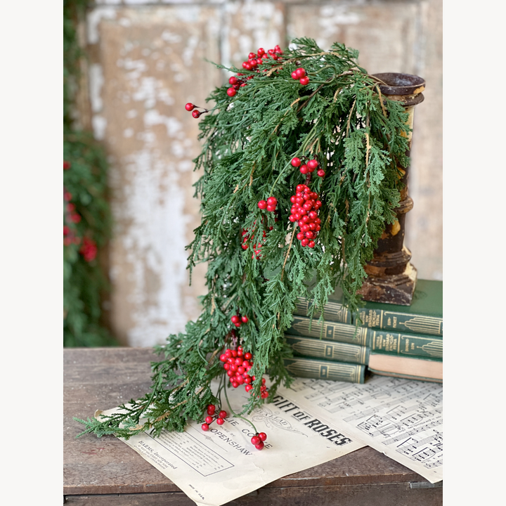 Decorative green garland with red berries on a rustic surface with books and newspaper.