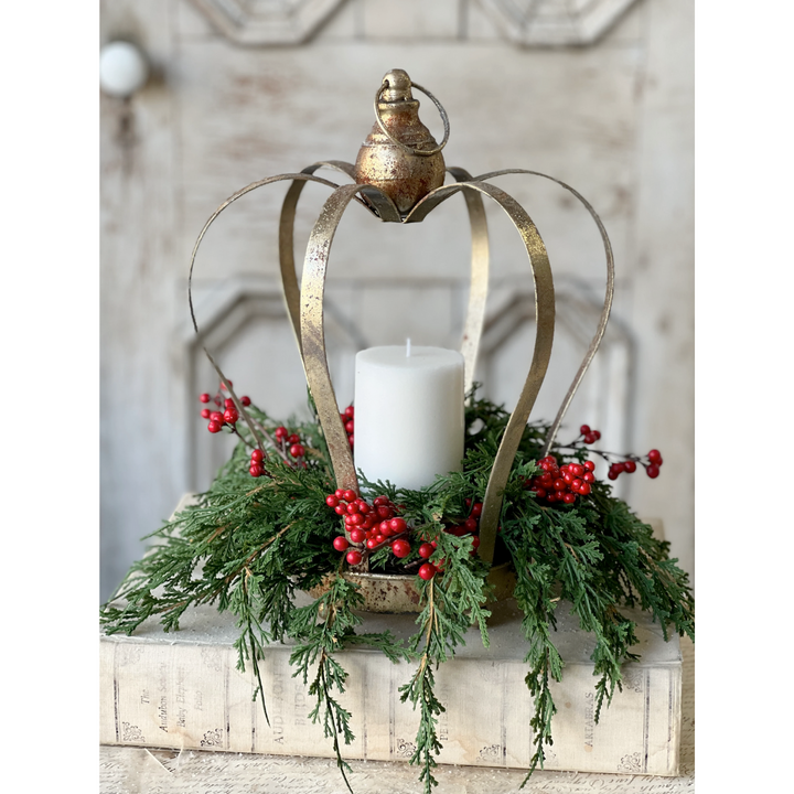 Decorative lantern with a candle, greenery, and red berries on a wooden surface.